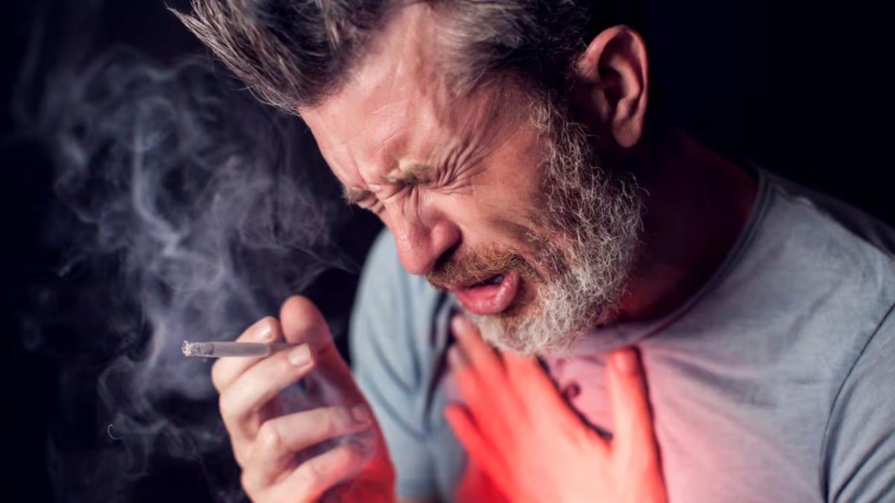 Hombre tomando su pecho, como si tuviera dolor y en su mano sostiene un cigarrillo