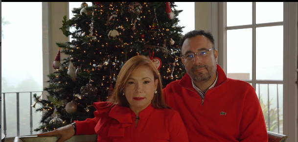 Luis Zelaya junto a su esposa vestidos de rojo y un arbol de navidad al fondo