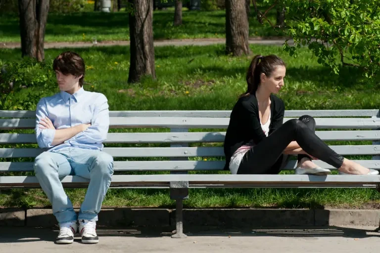 Imagen de una pareja distante que está sentada en una banca en un parque. 
