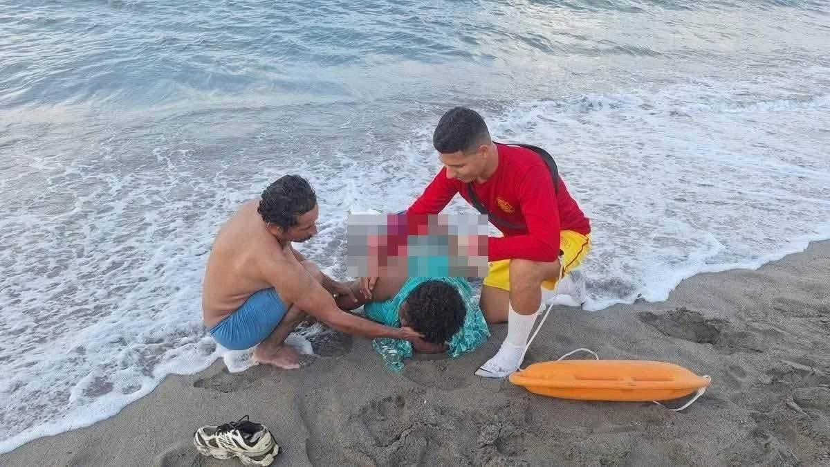 El cuerpo de María 'La Chichuy' a la orilla de la playa, mientras era auxiliada por su pareja y un elemento del Cuerpo de Bomberos. Foto: tomada de Facebook.